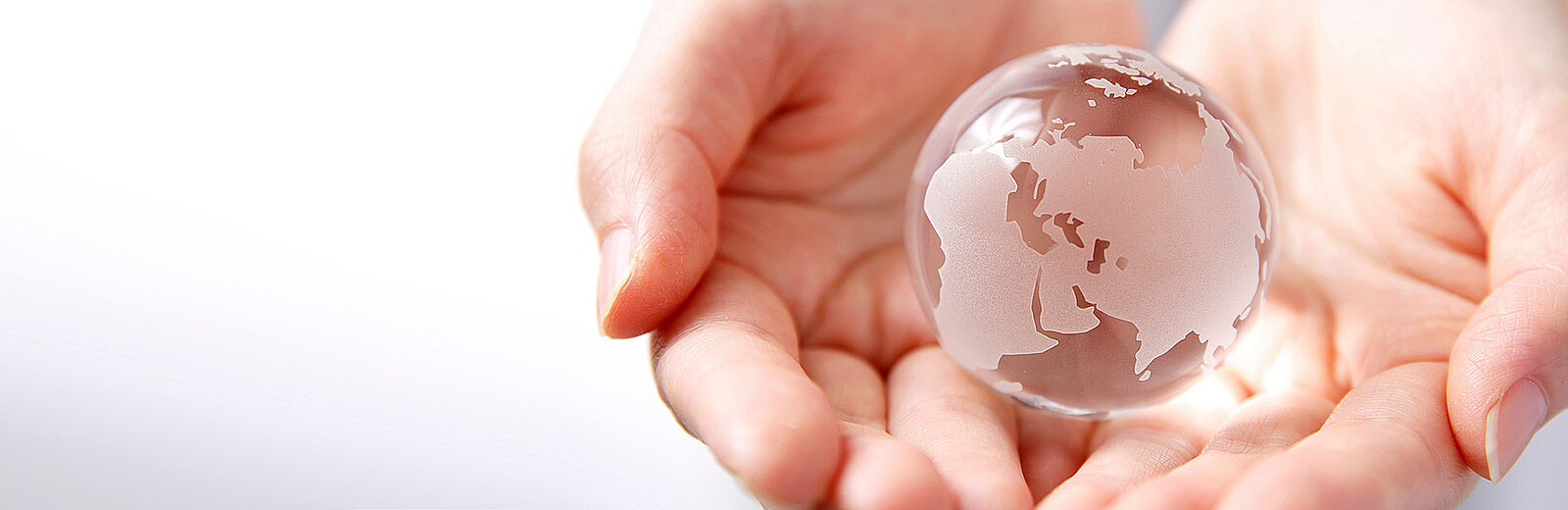 Zwei geöffnete Hände halten eine transparente Weltkugel – Symbol für Verantwortung, Offenheit und globale Verbundenheit.