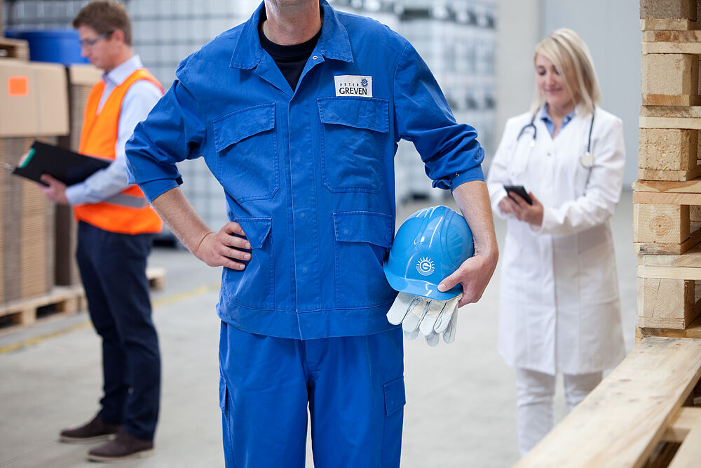 Arbeiter in blauer Schutzkleidung hält Helm und Handschuhe – Symbol für Arbeitsschutz und Sicherheit am Arbeitsplatz.