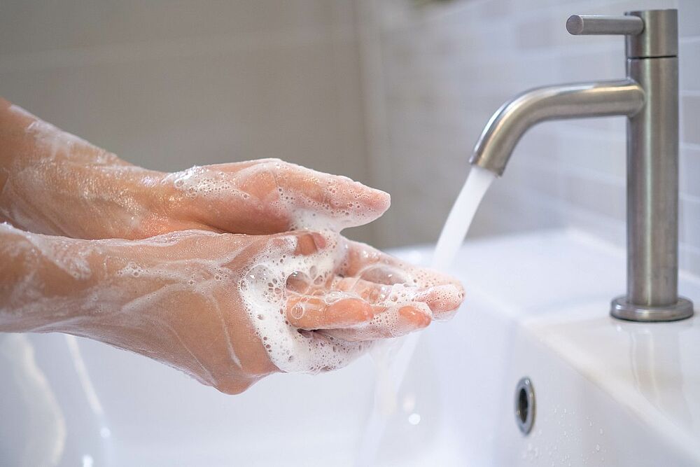 Person wäscht sich mit Seife gründlich die Hände unter fließendem Wasser – Symbol für Hygiene und Sauberkeit.